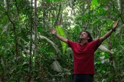 Young tourist man wearing red t-shirt raises his arms and looks up to the sky